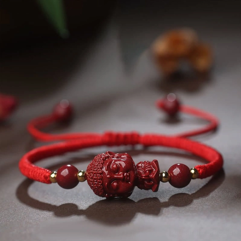 Double Buddha cinnabar charm red string bracelet flat lay with leaves