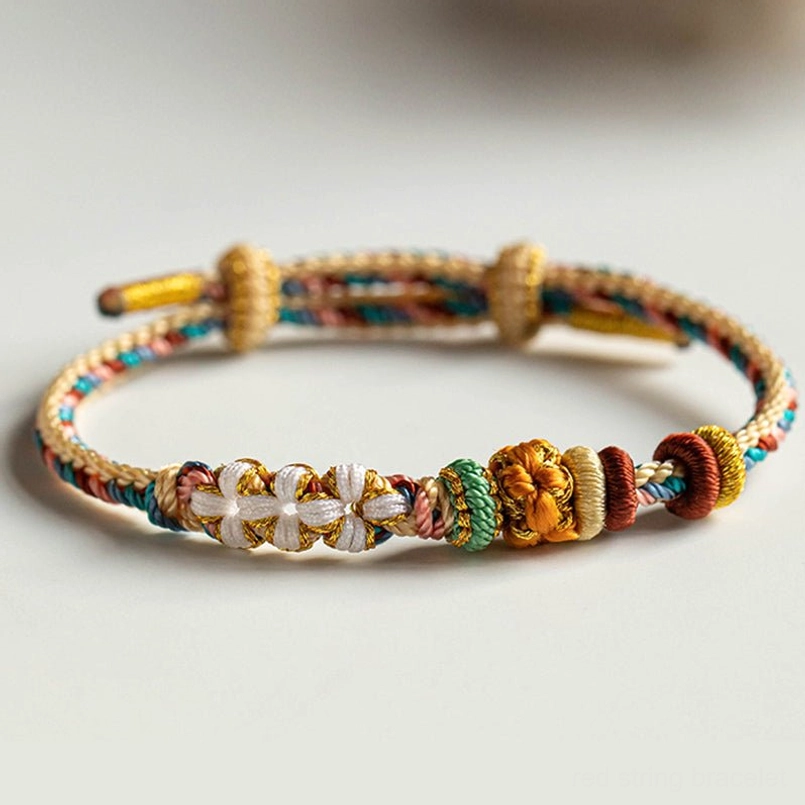 Colorful braided red string bracelet with disc knot and flower bead adjustable clasp on light cushion background