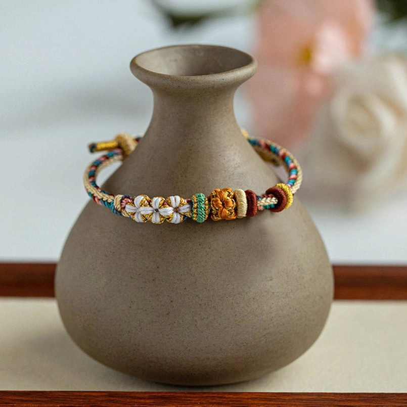 Artistic display of braided red string peach blossom bracelet with ceramic vase and floral background home decor