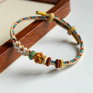 Handmade Dunhuang peach blossom braided red string bracelet with multicolor woven threads and flower knot on wooden tray