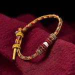 Handmade Dunhuang color luck braid string bracelet close-up view with ornate knot on maroon cloth