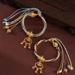 Two handmade Dunhuang red string bracelets with cloud lock pendants and bells on wooden surface