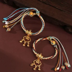 Two handmade Dunhuang red string bracelets with cloud lock pendants and bells on wooden surface