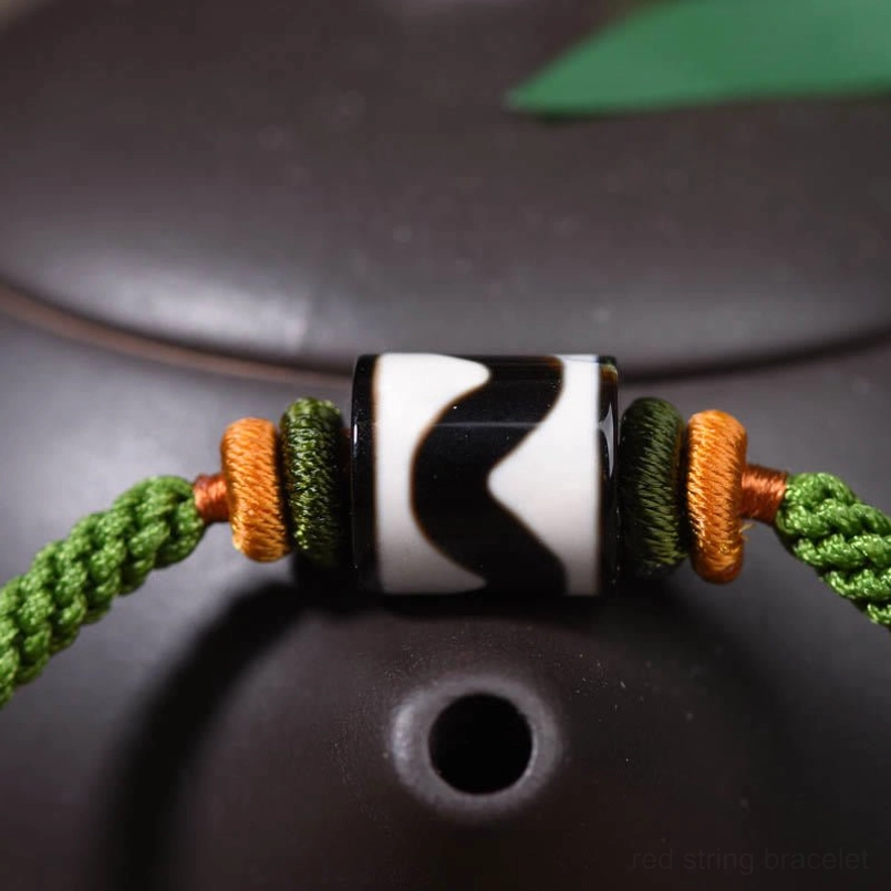 Close-up detail of handcrafted Tibetan Dzi bead with tiger stripe pattern and green woven cord