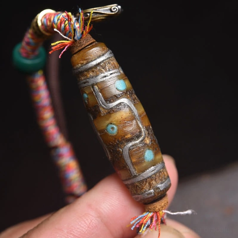 Close-up detail of Tibetan Dzi bead with silver and turquoise inlays attached to colorful craft cord