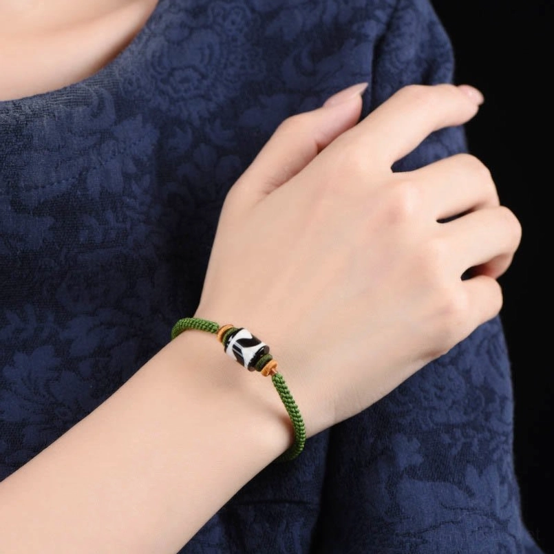 Tibetan Dzi bead green braided rope bracelet on textured background with adjustable design