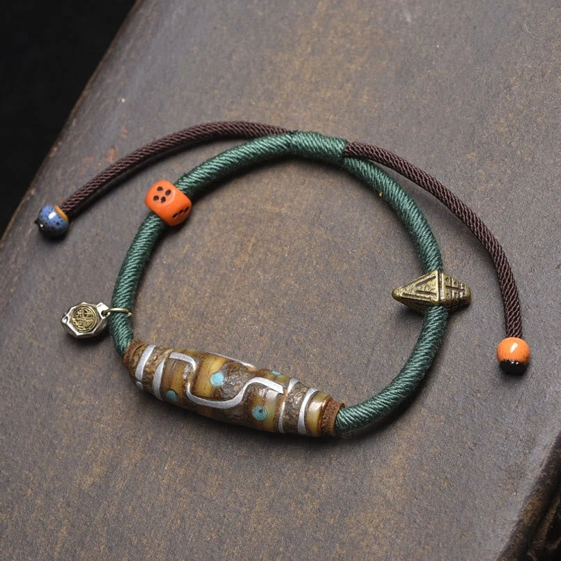 Green rope Dzi bead protection bracelet overhead flat lay with metal charms and colored stone beads
