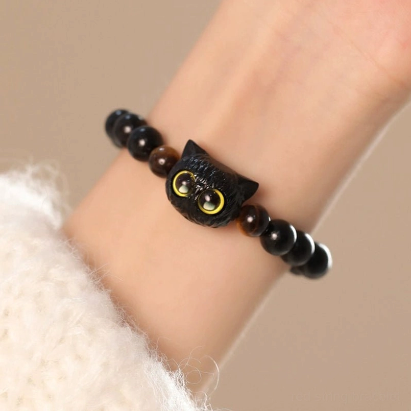 Ebony cat head red string bracelet worn on wrist with white sweater background
