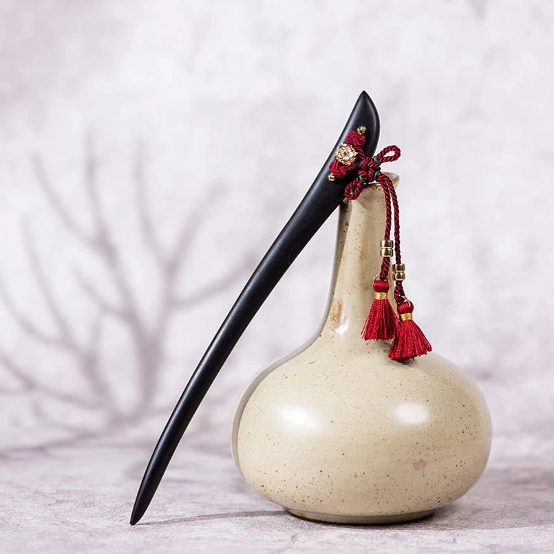 Ebony tassel hairpin with red knot displayed on ceramic vase tabletop
