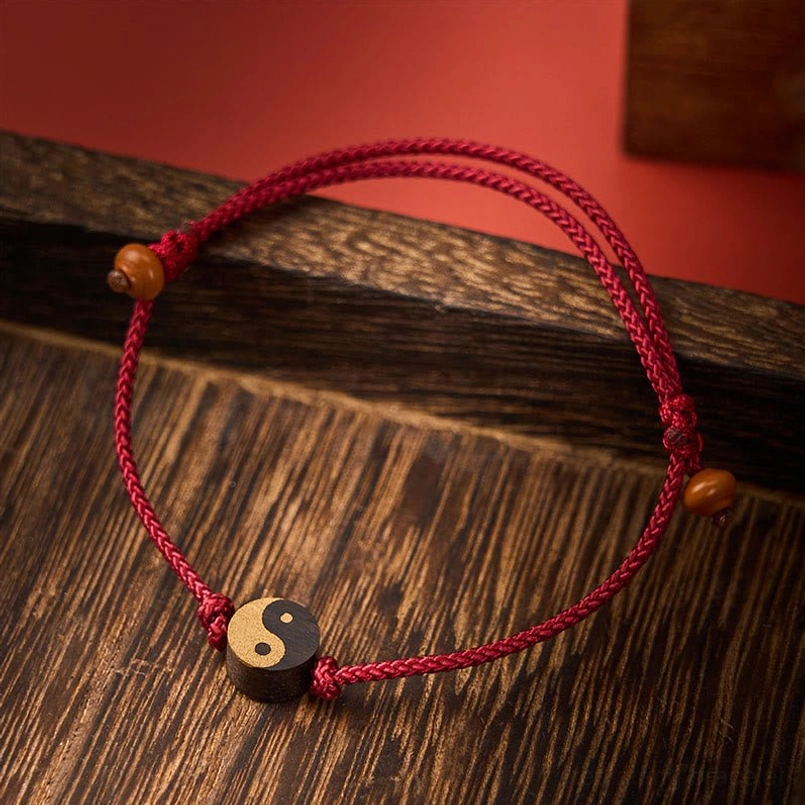 Red Ebony Yin Yang bracelet with adjustable string on dark wooden surface