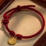 Eight thread peace knot Fu character red string bracelet with gold charm on wooden display