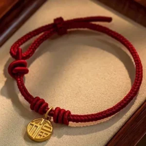 Eight thread peace knot Fu character red string bracelet with gold charm on wooden display
