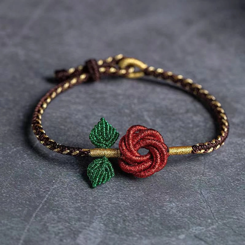 Handmade eight thread peace knot red rose bracelet with brown-gold braided cord and green leaves on stone desktop