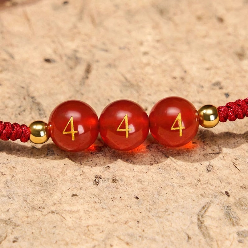 Close-up of Angel Number 444 engraved red agate beads with woven red cord and spacers