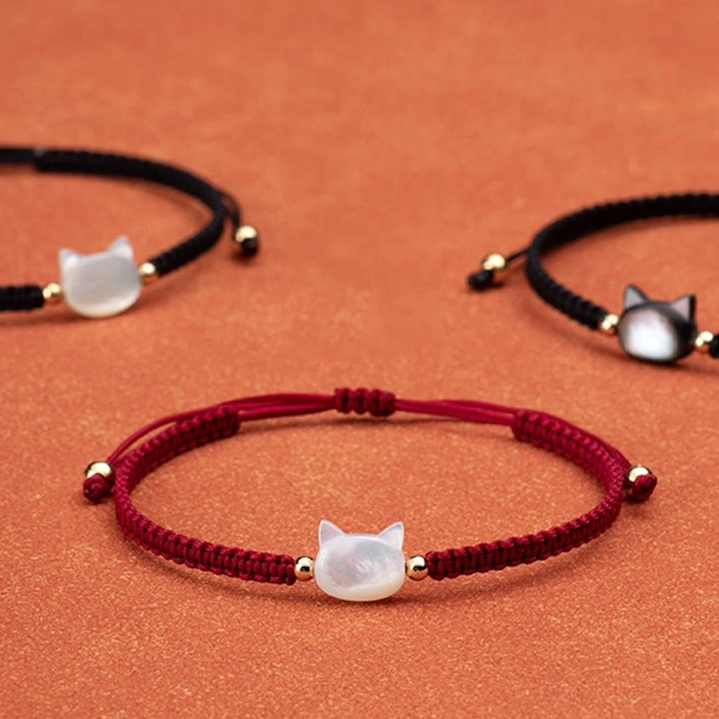 Faceless cat shell red string bracelet collection flat lay with white and black rope options