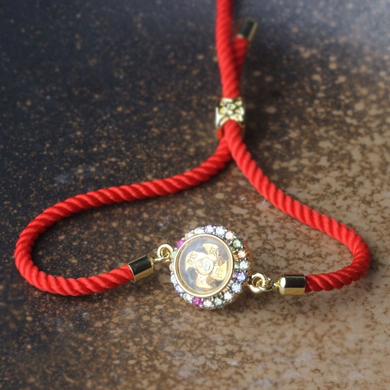 Rotating feng shui red string bracelet with transparent crystal-inlaid charm on dark surface