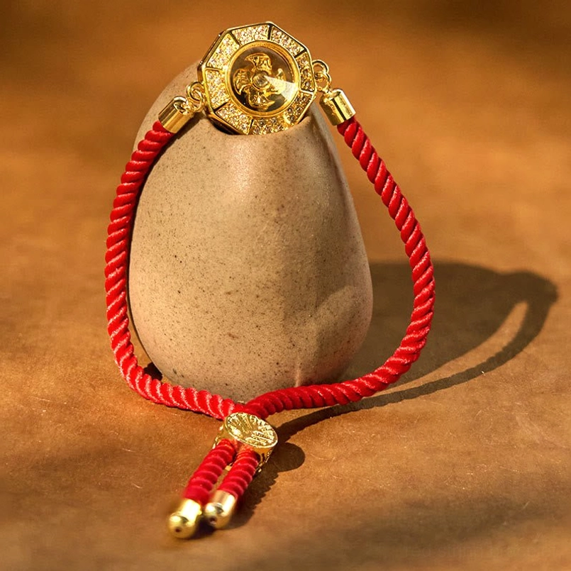 Three-quarter view of copper brass red string windmill bracelet with rotatable octagonal charm and twisted red rope