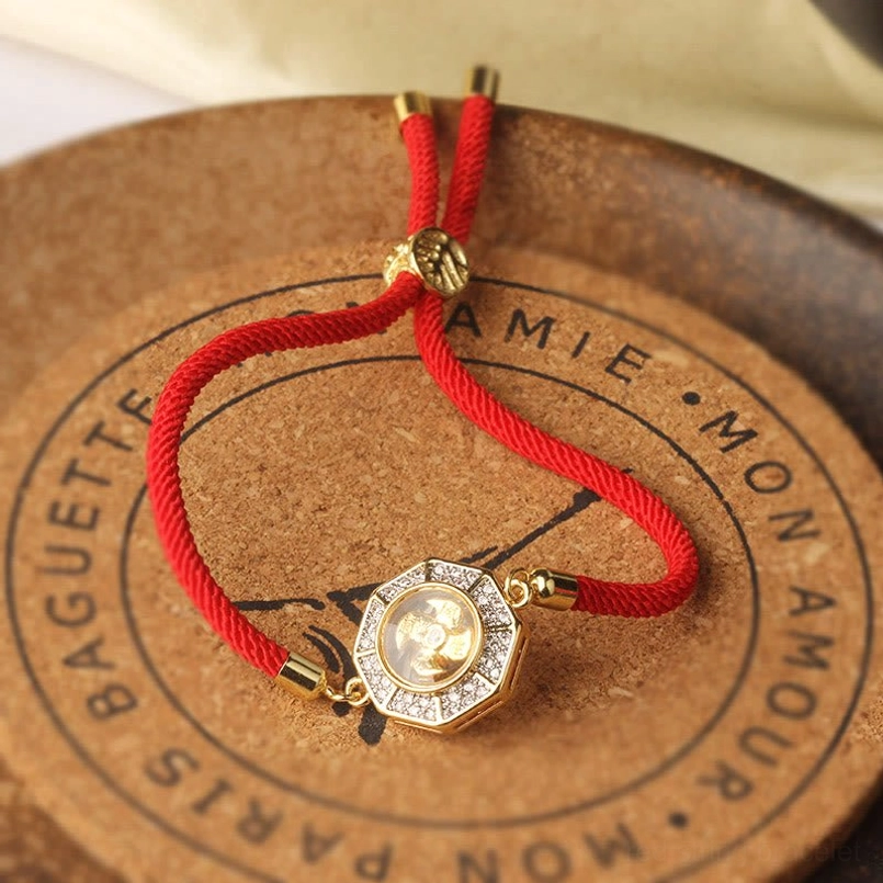 Top-down flat lay of feng shui windmill red string bracelet on cork coaster with adjustable gold toggle clasp