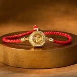 Rotating feng shui red string windmill bracelet with octagonal copper charm and braided red rope on gold display platform