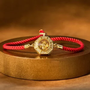 Rotating feng shui red string windmill bracelet with octagonal copper charm and braided red rope on gold display platform