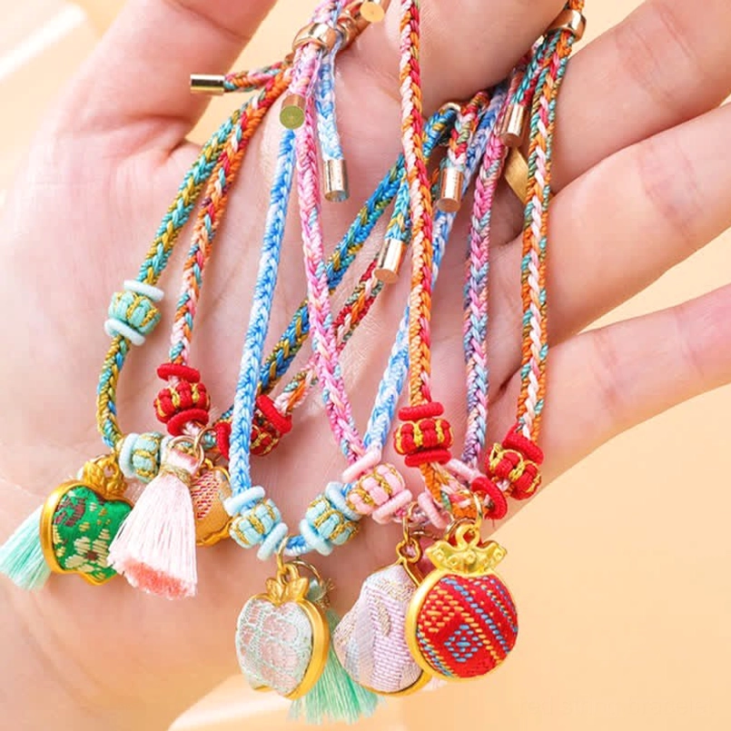 Five-color braided cord luck bracelets with embroidered and enamel charms piled in palm of hand