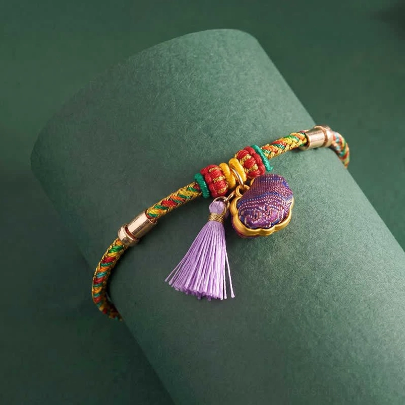 Rainbow-colored braided festival bracelet with purple tassel ornament on display stand