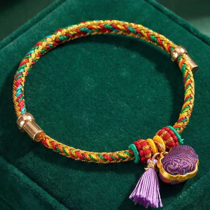 Adjustable five-color woven cord bracelet with fabric pendant on dark green velvet background