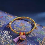Five-color lucky bracelet with Chinese lock charm pendant resting on dragon-patterned Song Brocade fabric