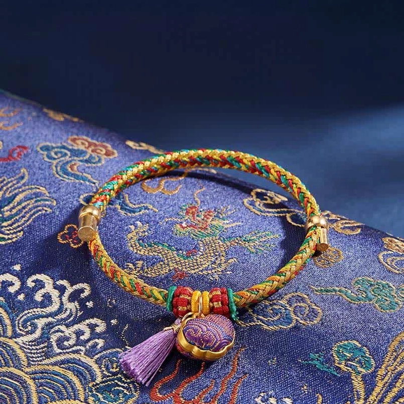 Five-color lucky bracelet with Chinese lock charm pendant resting on dragon-patterned Song Brocade fabric