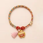 Five-color handwoven red string bracelet with embroidered apple charm and pink tassel on light pink background