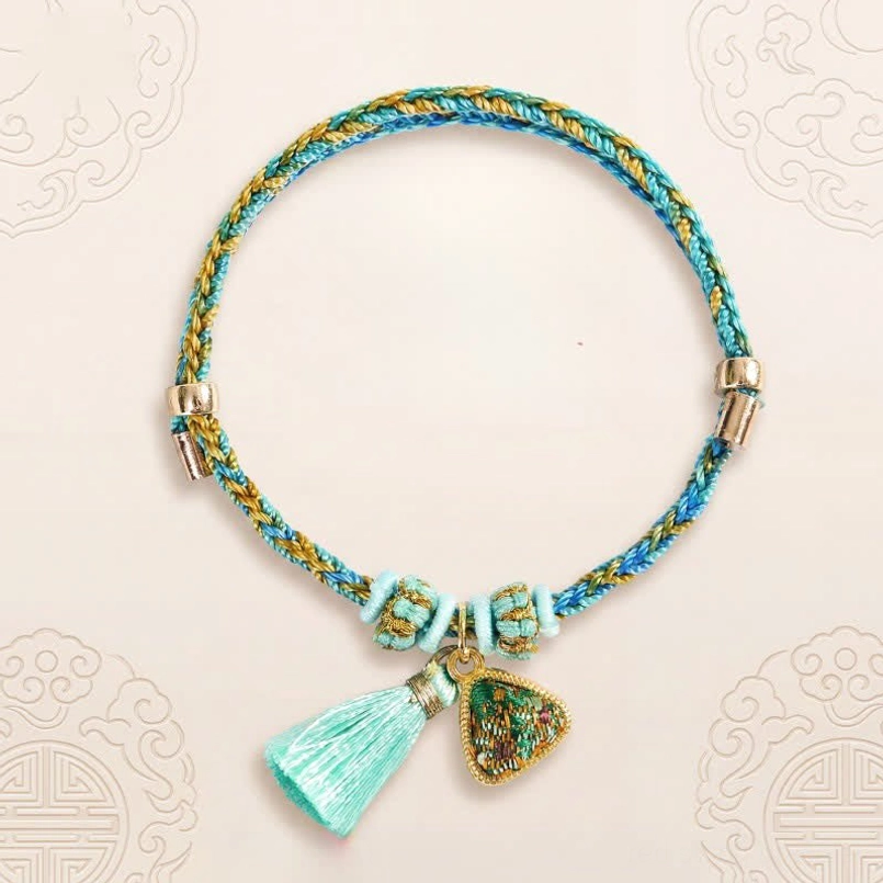Hand-woven Chinese luck bracelet with blue yellow braided rope matching tassel and protection pendant against cloud pattern background
