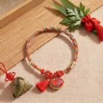 Five-color song brocade lucky bracelet with embroidered lock charm pendant, displayed on bamboo mat with festive ornaments