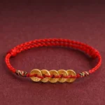 Five copper coins red string braided bracelet with colorful woven knot closure on dark red fabric