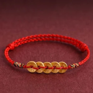 Five copper coins red string braided bracelet with colorful woven knot closure on dark red fabric