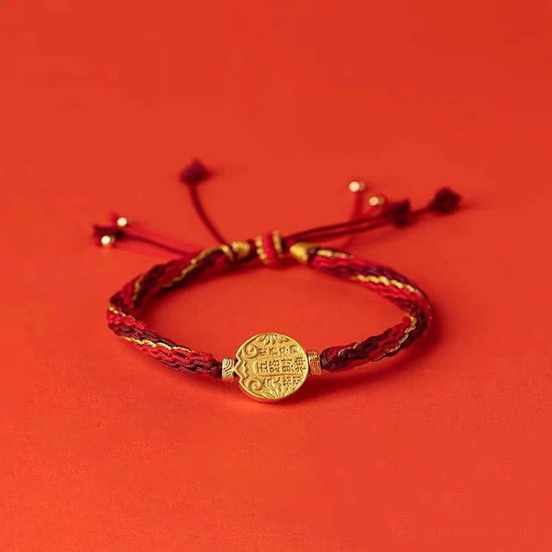 Red string wealth protection bracelet flat lay showing detailed gold charm inscribed with five directions symbols