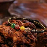 Five Directions wealth agate braided bracelet in black cord with five polished gemstone beads on wooden carving background