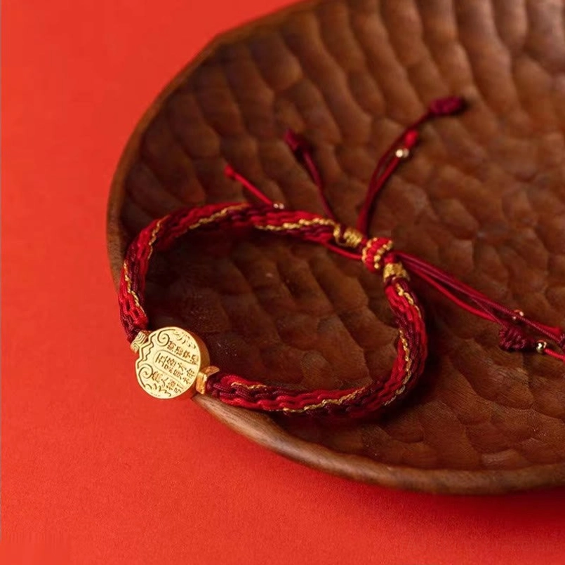 Five Directions wealth red string bracelet with reincarnation knot and gold charm, handmade protection bracelet displayed on textured tray