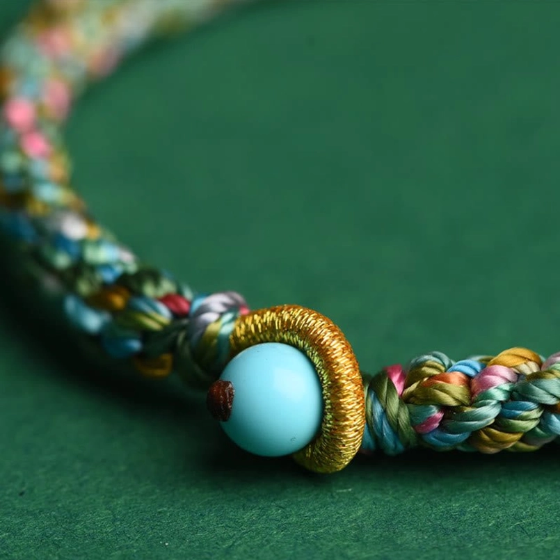 Macro close-up of golden woven knot and large turquoise bead clasp on multicolor lucky bracelet