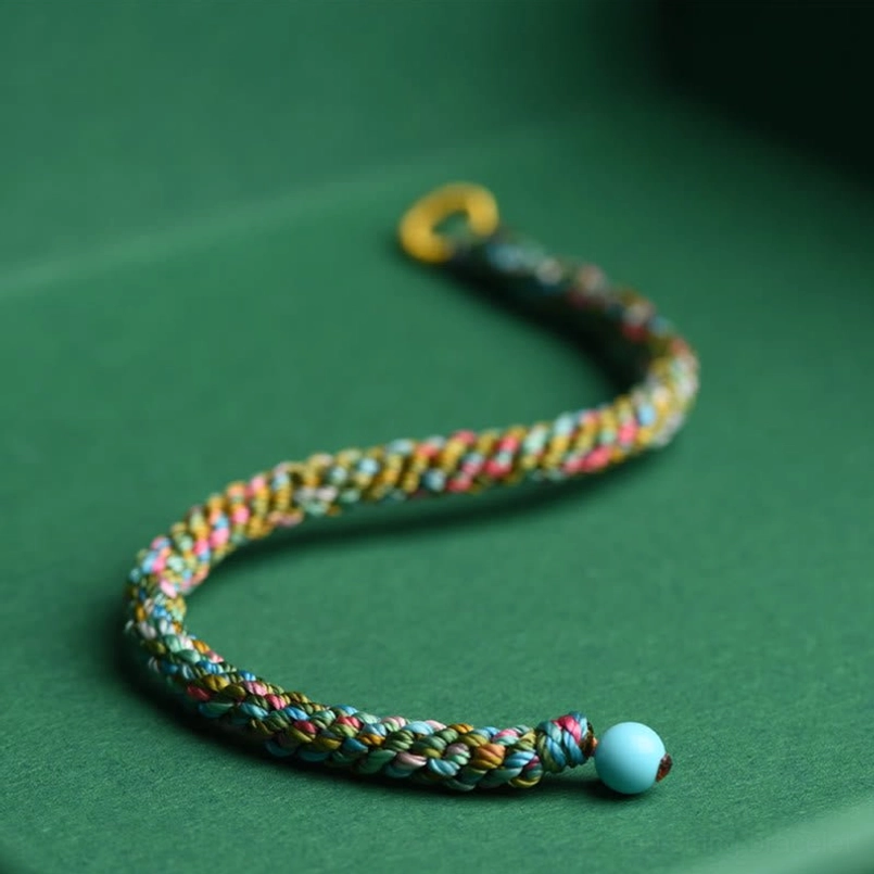 Curved multicolor braided lucky bracelet with dual turquoise beads on dark tabletop, five element design