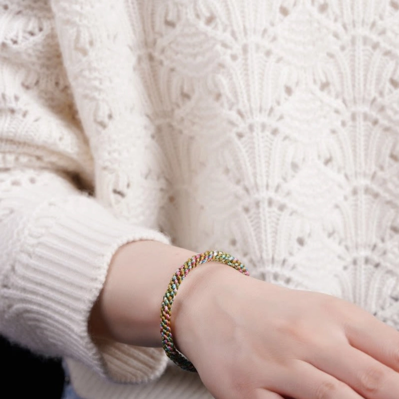 Multicolor braided lucky bracelet on wrist with white knit sweater, casual daily wear style for protection and luck
