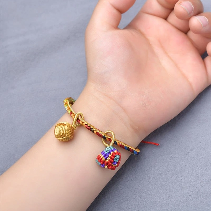 Handmade five element red string bracelet with golden ball charm on hand gray fabric