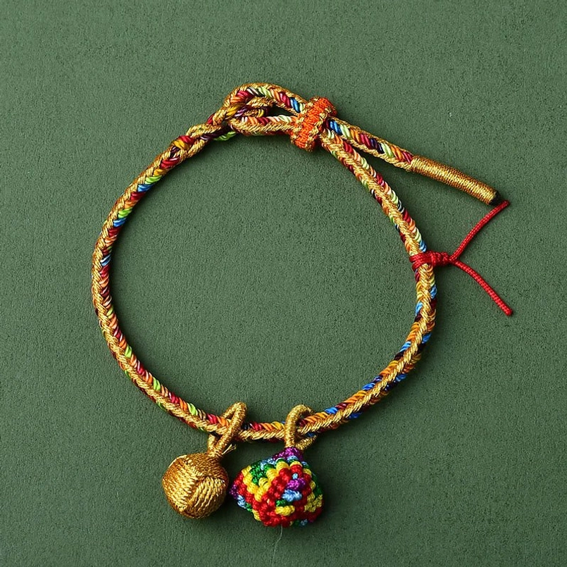 Hand-woven multicolor red string bracelet with golden thread and dual charms dark background