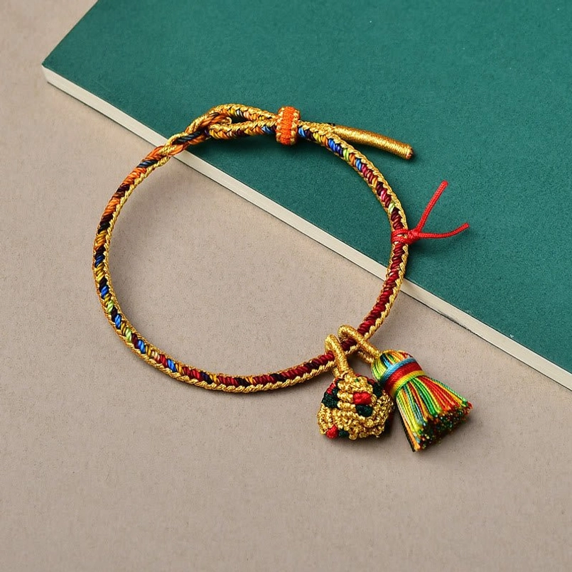 Hand-woven lucky bracelet with gold threads and decorative pendants on dark green book