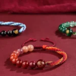 Five elements reincarnation knot crystal agate bracelets assortment with braided red cord on velvet background