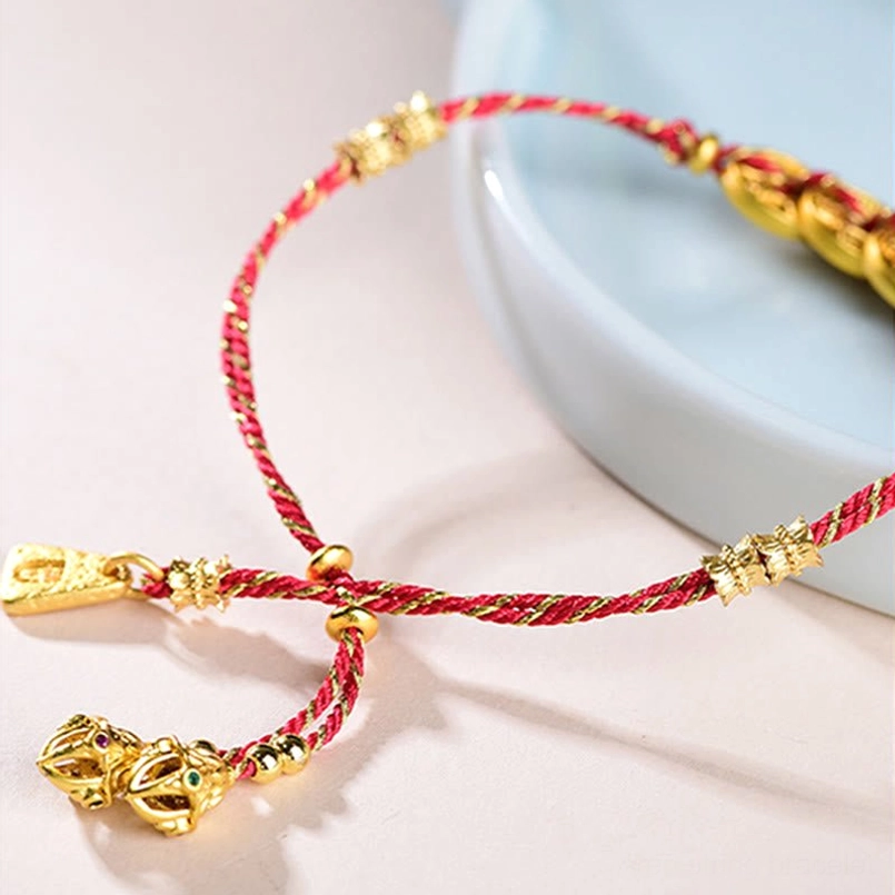 Twisted red and gold woven rope bracelet with gold-plated beads on ceramic backdrop