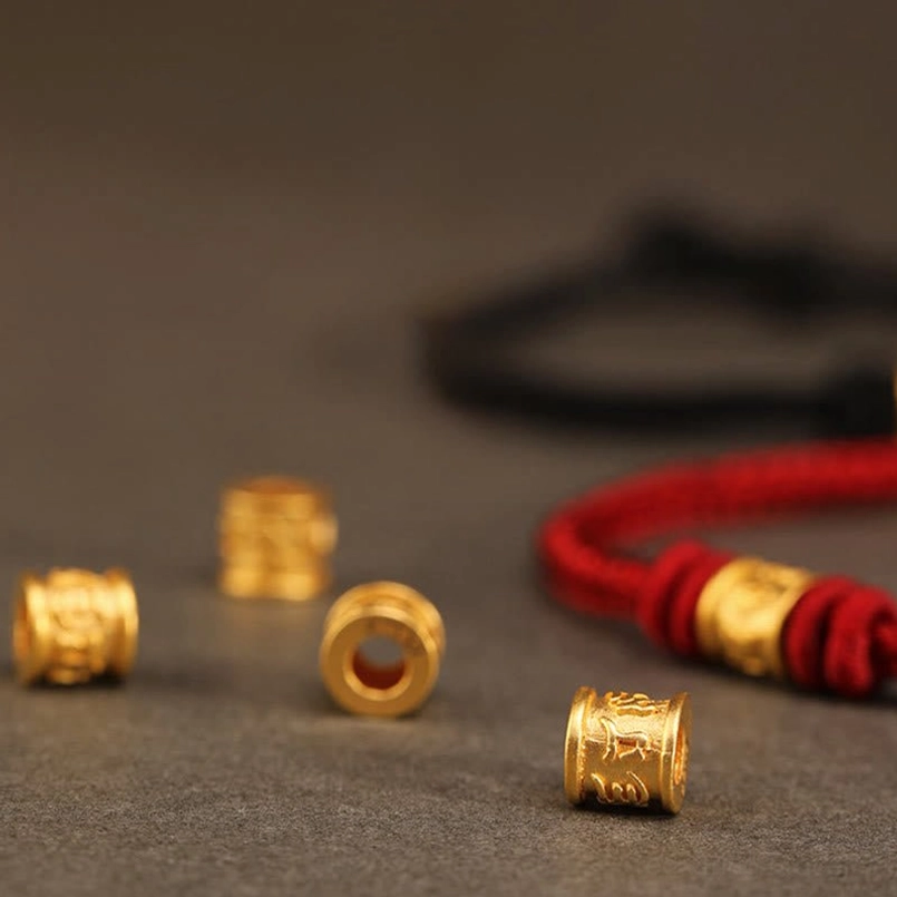 Flat lay close up of 999 gold Om Mani beads and partial red bracelet