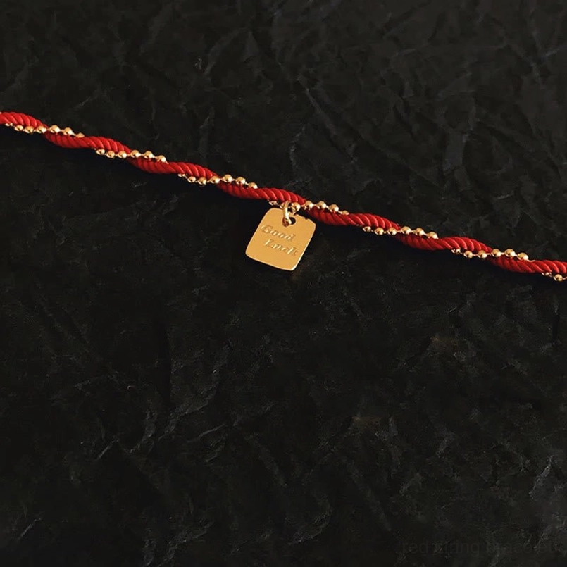 Top down flat lay red rope bracelet with square engraved Good Luck tag