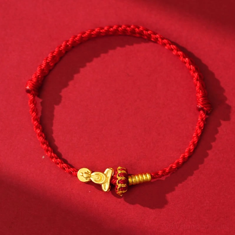Overhead view of red string bracelet with Formless Buddha charm and gold vajra ornament on red background