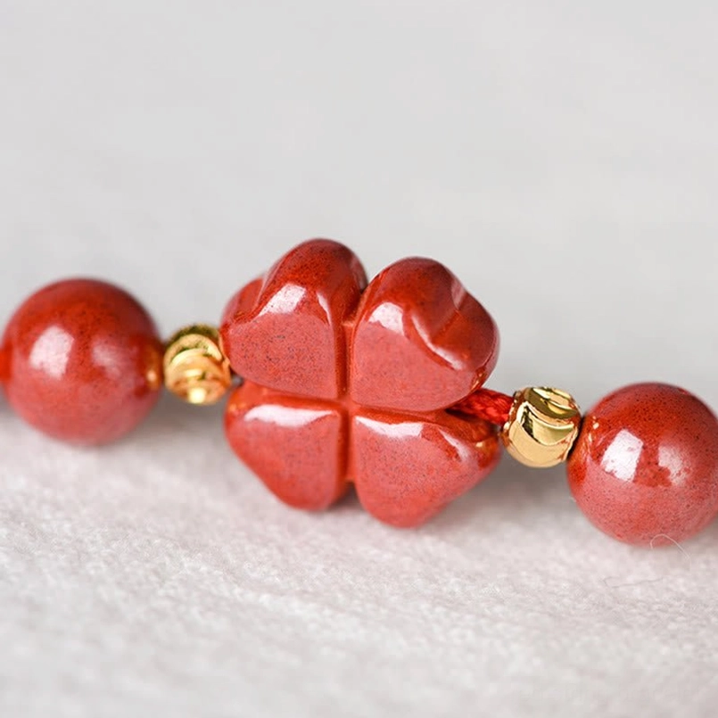 Four-leaf clover cinnabar charm with gold spacer beads and round bead accents close-up
