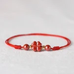 Four leaf clover cinnabar red string bracelet with gold spacer beads on light grey background